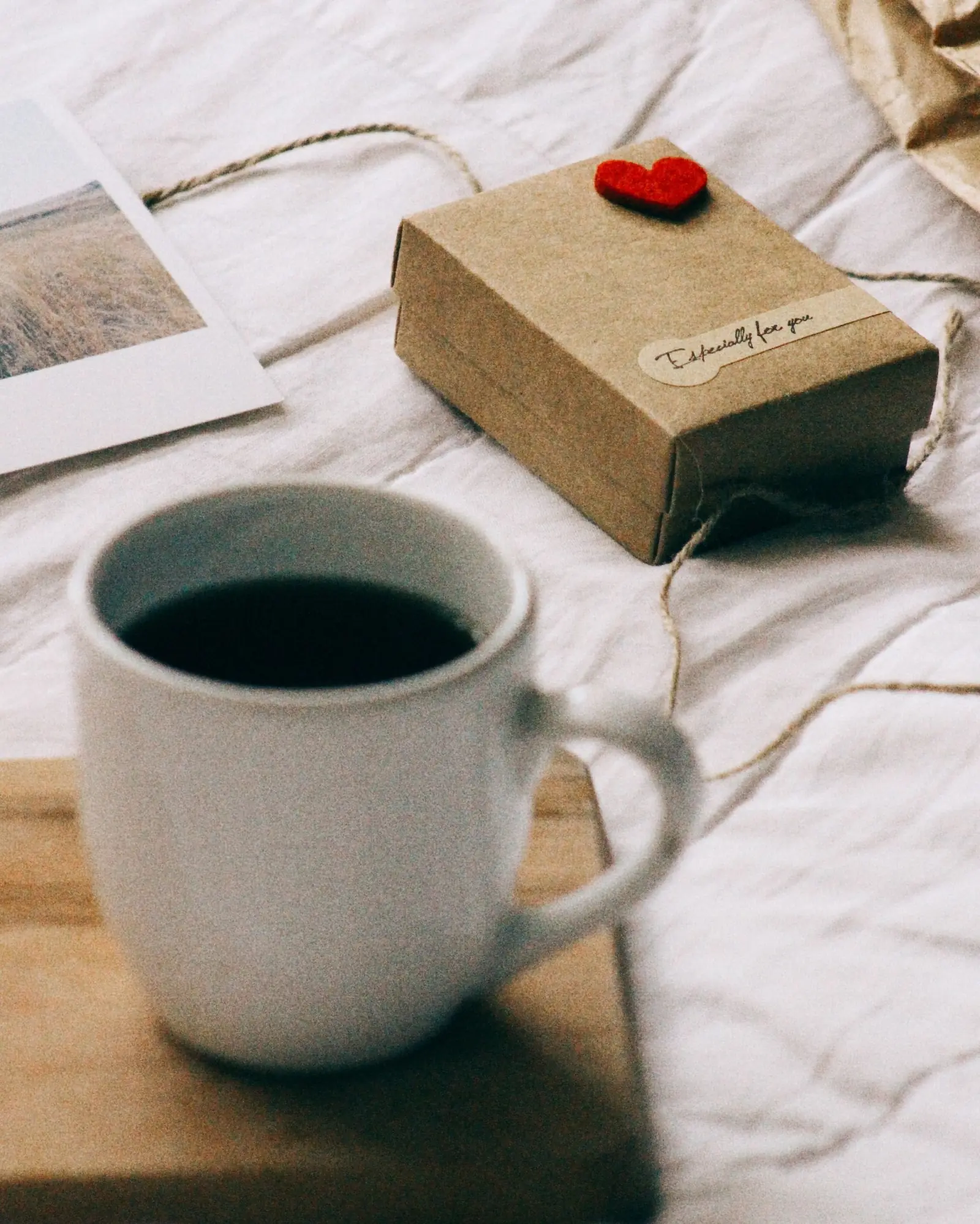 A wrapped gift beside a cup of coffee and a pastry on a wooden table.