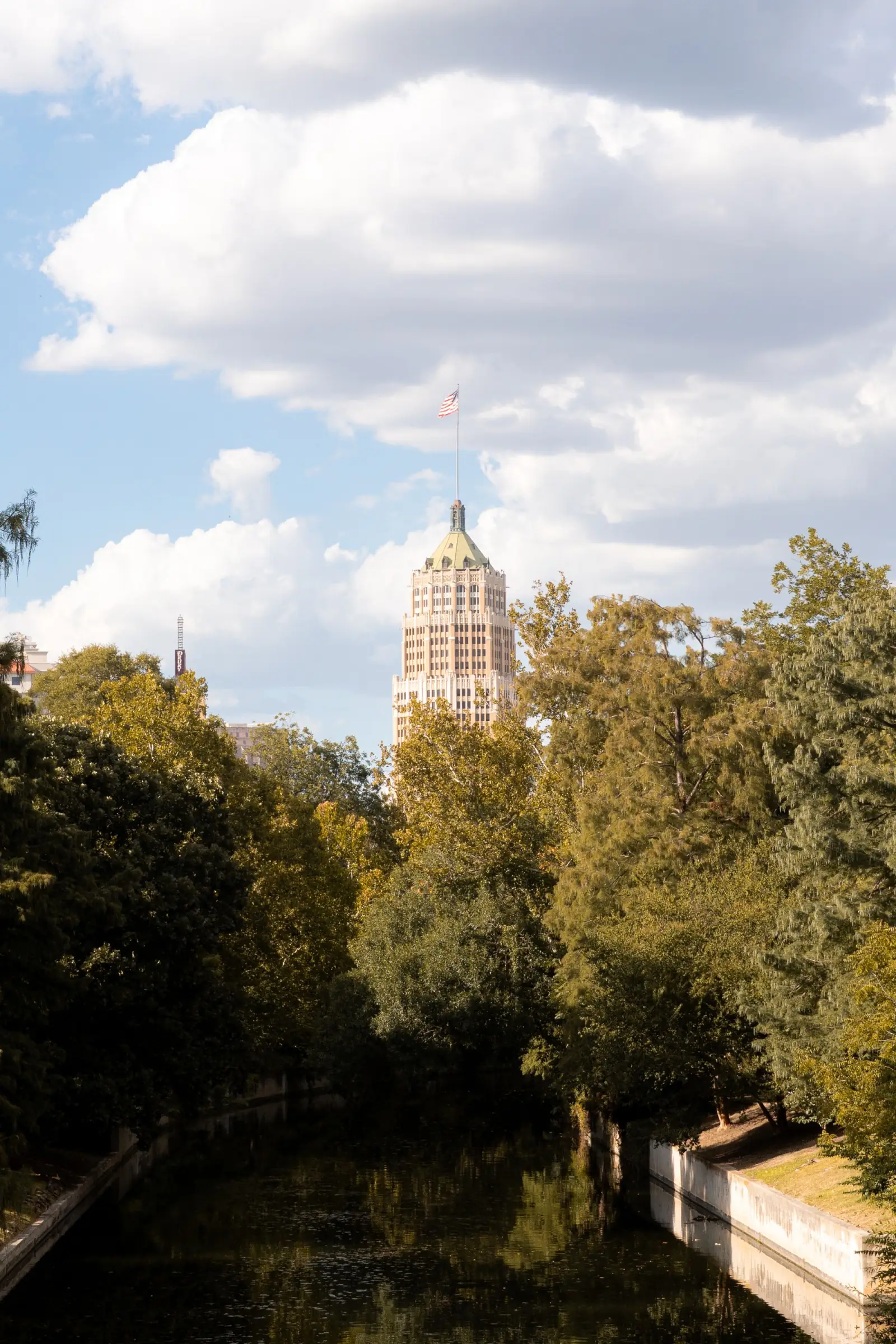 The Tower Life Building rising above trees along the San Antonio River.