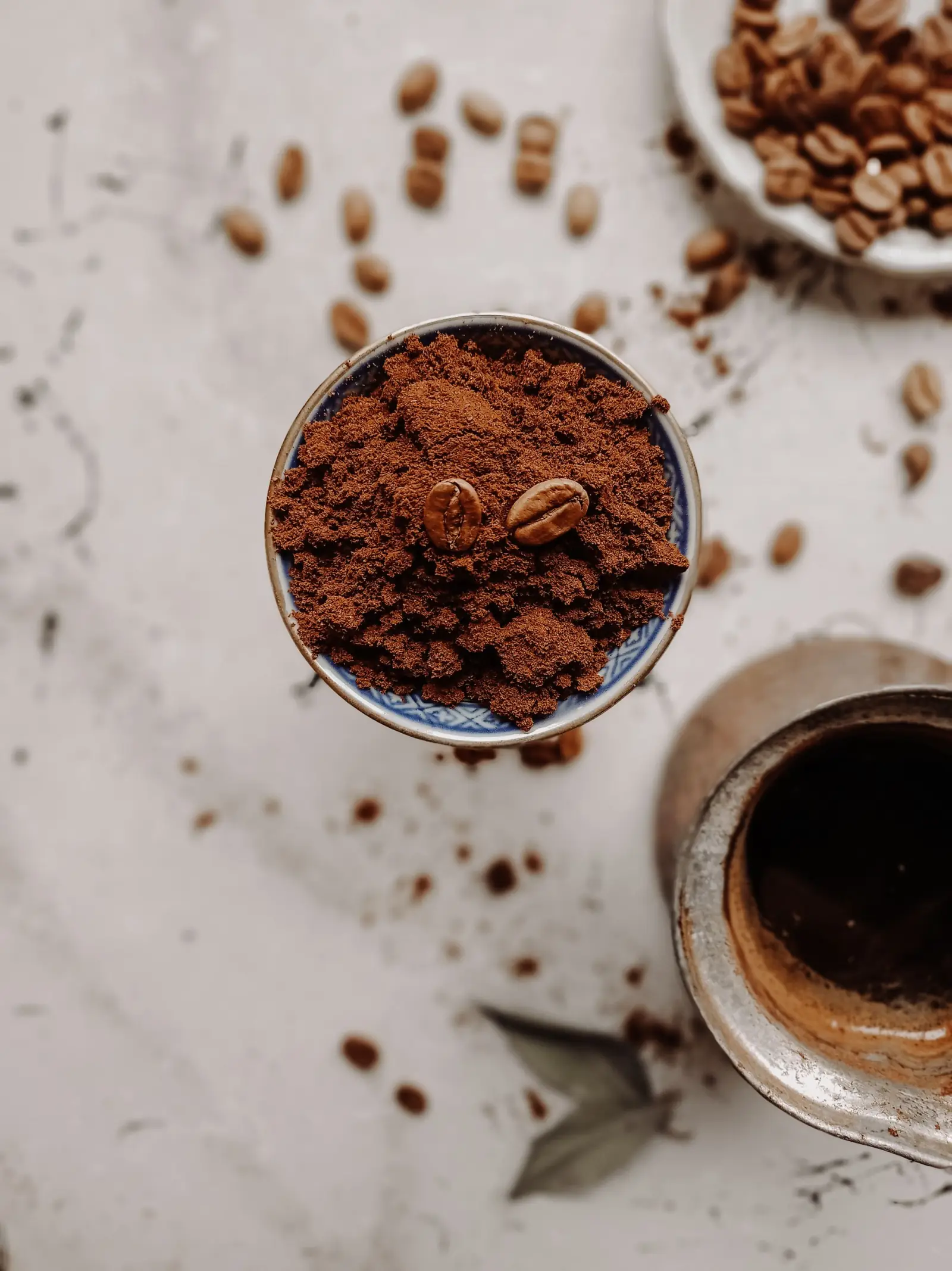 Whole coffee beans next to a bowl of ground coffee.