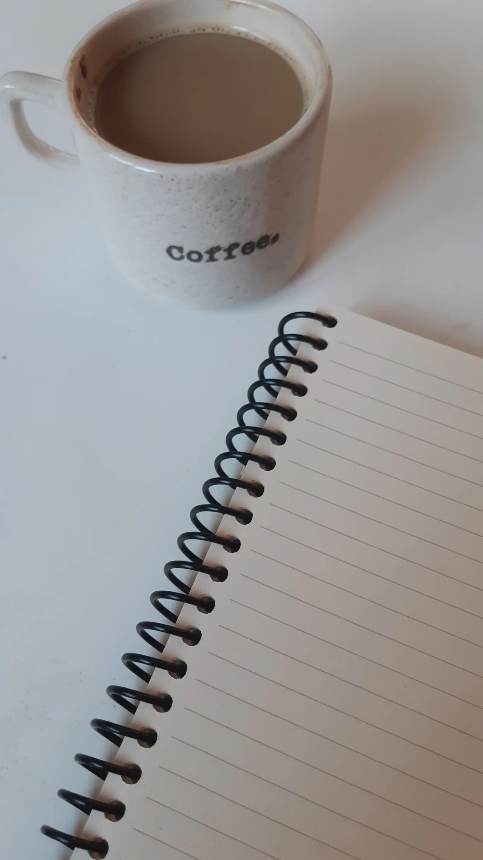 A coffee mug beside an open notebook and a pen.