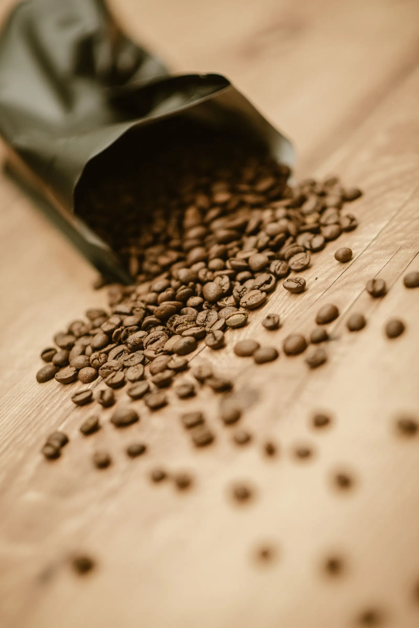 Roasted coffee beans spilling from an open bag onto a wooden table.